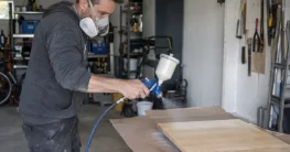 Heimwerker übt mit einer Lackierpistole auf einem Probebrett aus Holz