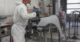 Lackierer im Schutzanzug lackiert einen grundierten Kotflügel mit einer HVLP-Lackierpistole