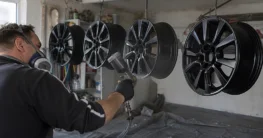 Vier Alufelgen hängen an Haken in einer Garage und werden schwarz lackiert